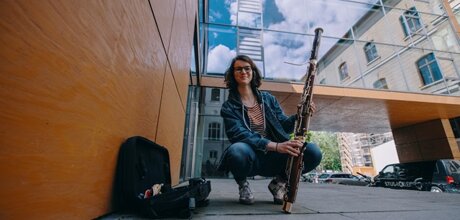 Mareike hockt vor dem HMT-Gebäude und hält ihr Fagott in der Hand.