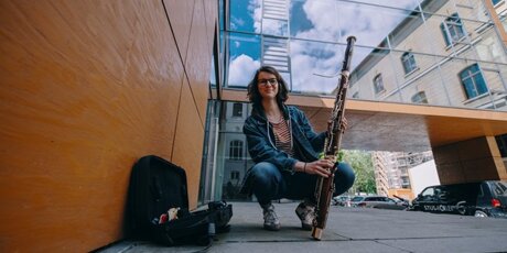 Mareike hockt vor dem HMT-Gebäude und hält ihr Fagott in der Hand.