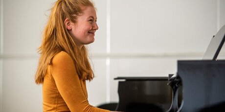 Clarissa sitzt am Klavier, spielt und lacht.