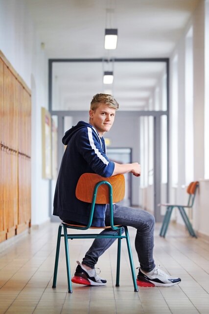 Florian sitzt auf einem Stuhl im Flur der Staatlichen Studienakademie Glauchau.